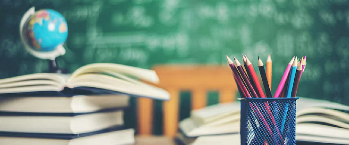 Een stapel boeken en een wereldbol op een houten schoolbank voor een krijtbord, als symbool voor persoonlijke groei, leren op eigen tempo en de brede ontwikkelmogelijkheden binnen Librijn Ontwikkel à la Carte.